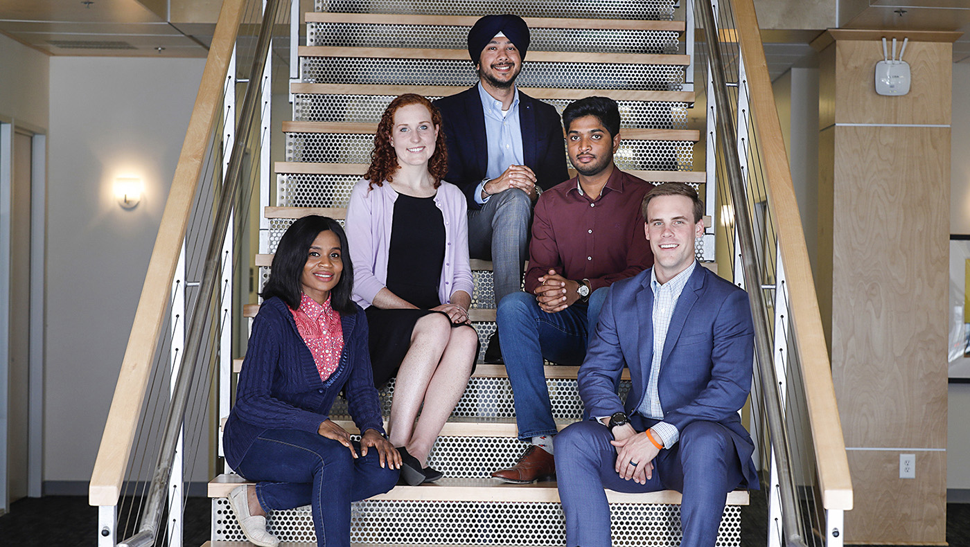 A group of five diverse graduate students post together on a staircase