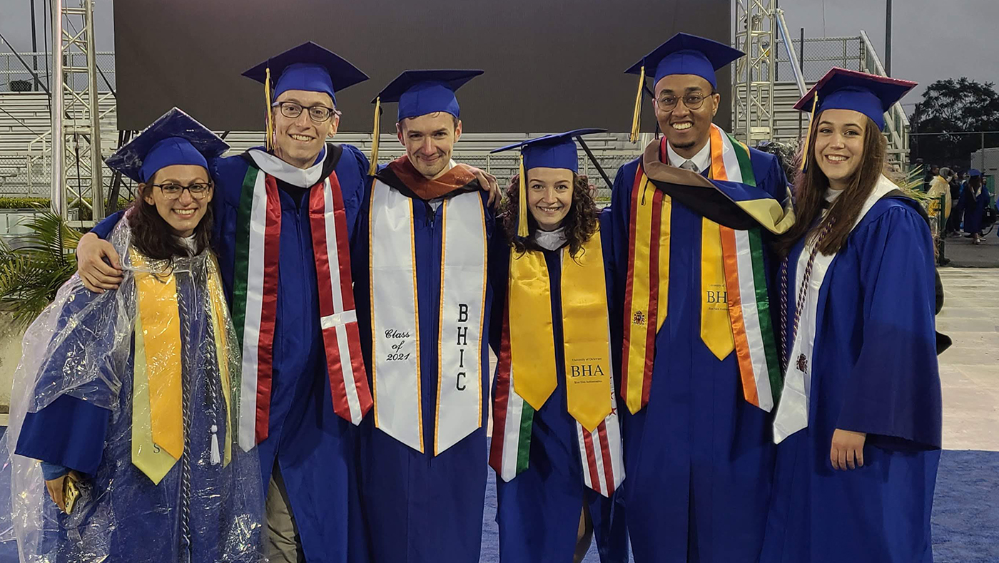 Six graduating students stand together smiling in their robes.
