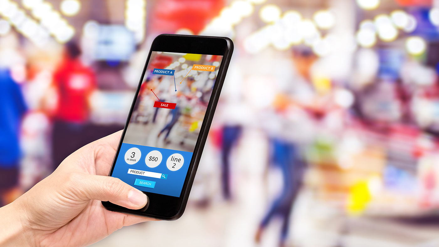 Photo of a mobile phone being used to compare prices with a blurred background showing a busy store